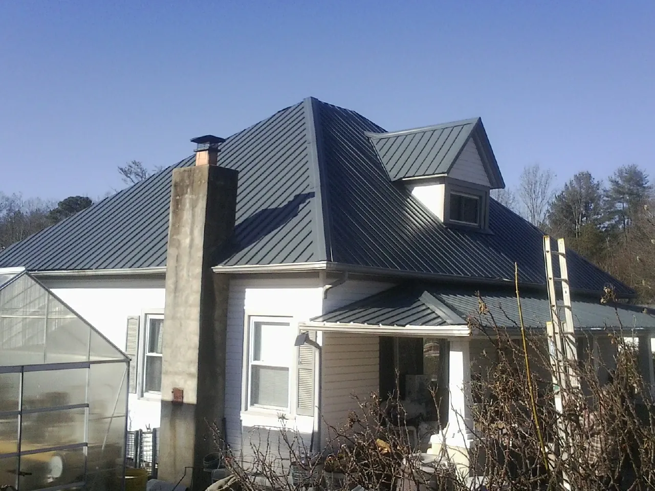 Dark blue standing seam metal roof on a white farmhouse with dormer — Slate & Tile Roof Repair by Roofing Brothers in Castle Dale
