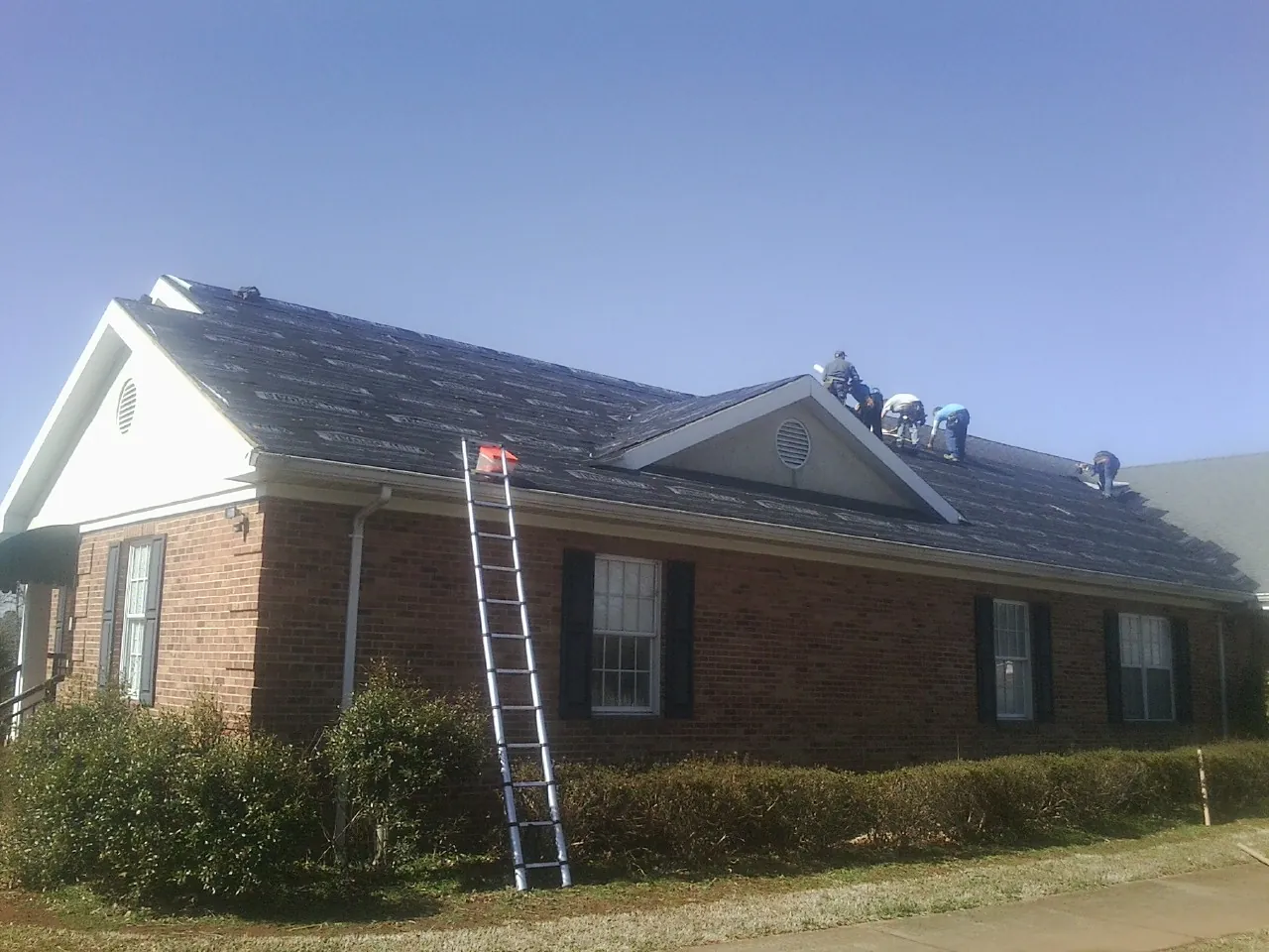 Crew tearing shingles off a brick ranch roof with a ladder set — Emergency Roof Repair work by our crew in Castle Dale