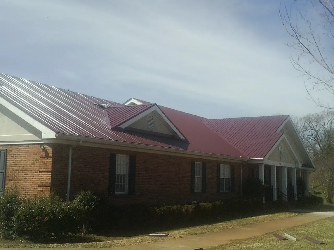 Red metal roof with gabled entries on a long brick building, from a Hail Damage Roof Repair job in Castle Dale