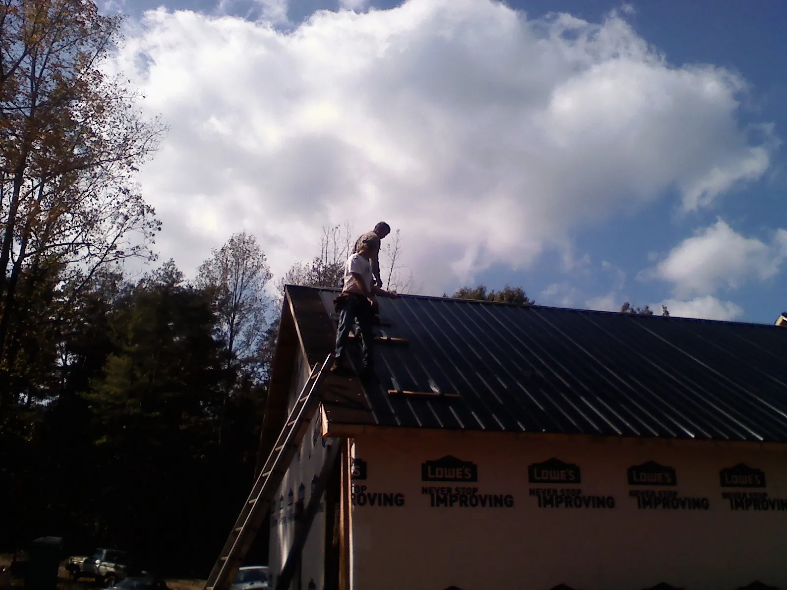 Roofer fastening dark metal panels high against a cloudy sky, from a Roof Inspection job in Castle Dale