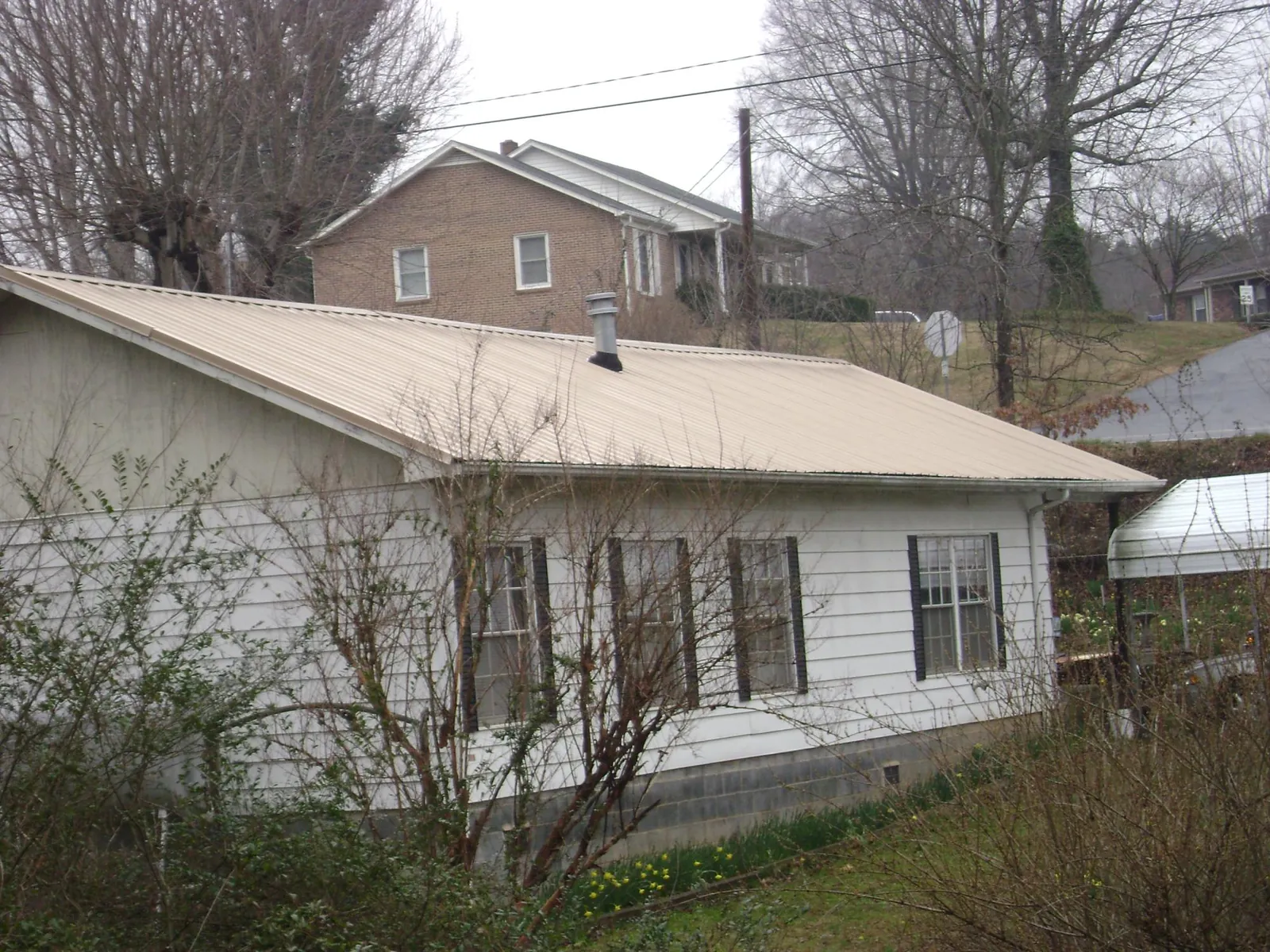 Tan metal roof on a white sided house set into a hillside — Commercial Roofing by Roofing Brothers in Castle Dale